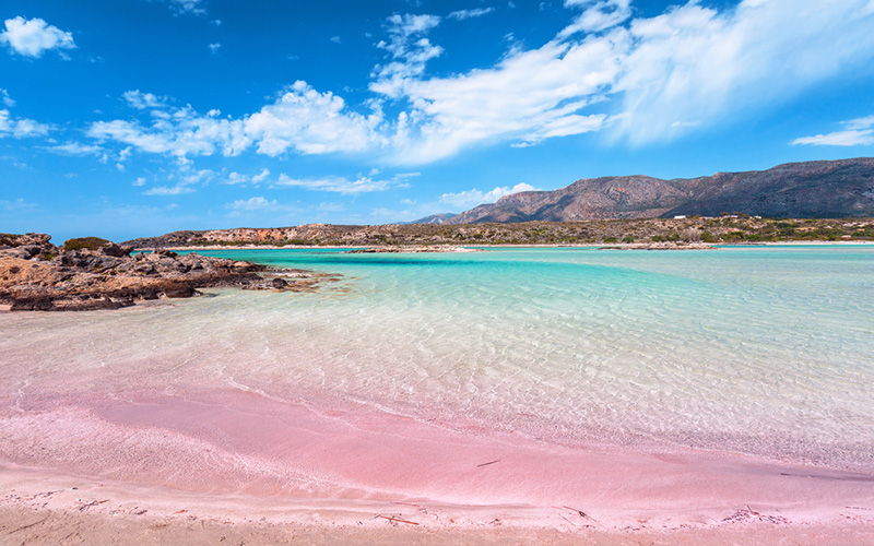 Roze strand met blauw water en hoge rotsen