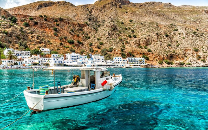 Un petit bateau naviguant sur les eaux turquoises de la Crète, avec la côte en arrière-plan