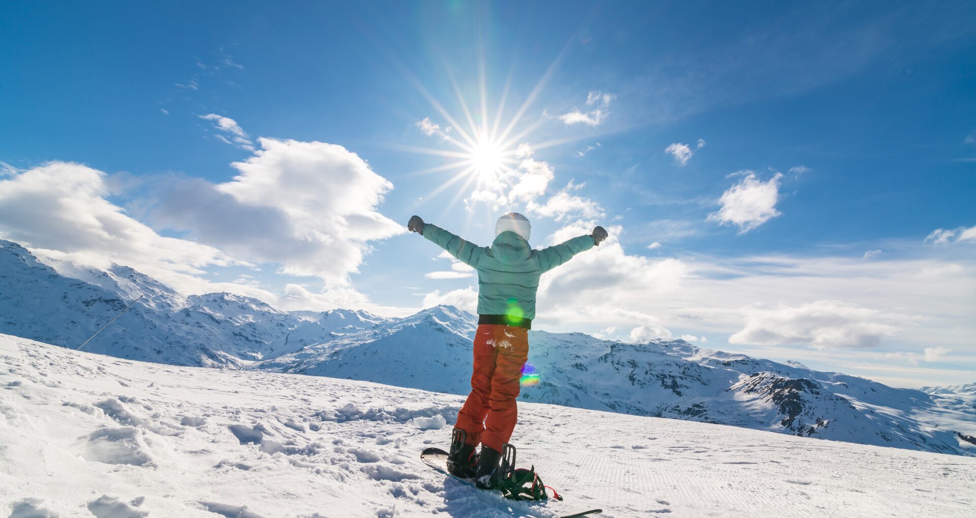 Un skieur de dos levant les bras en l'air, face aux montagnes enneigées