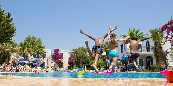 Drie kinderen springen tegelijk in het zwembad bij een hotel.