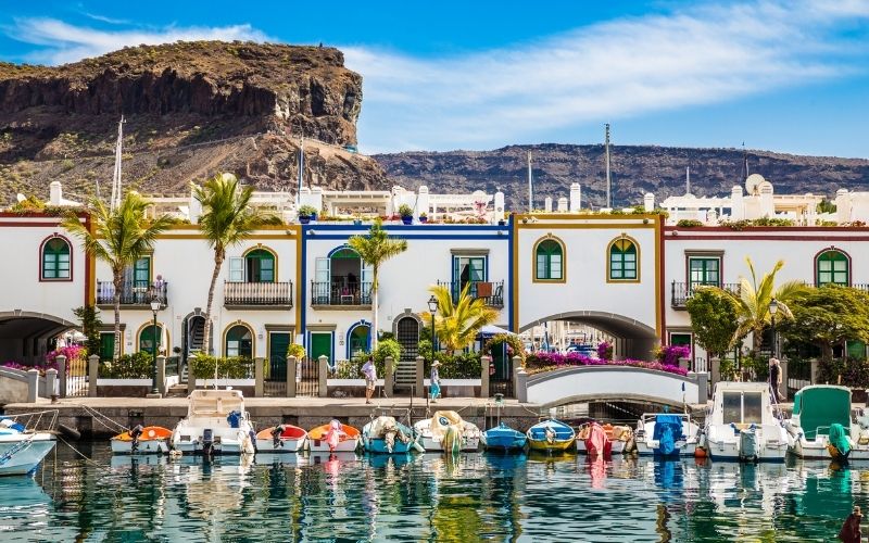 Jachthaven op Gran Canaria met bootjes en kleurrige huizen en bergen op de achtergrond
