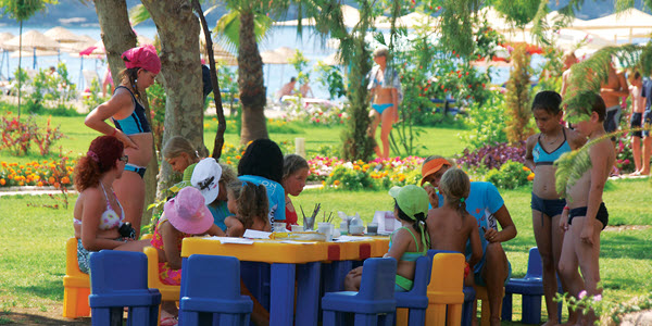 Kinderen spelen buiten aan een gekleurde kindertafel, onder begeleiding van animatoren.