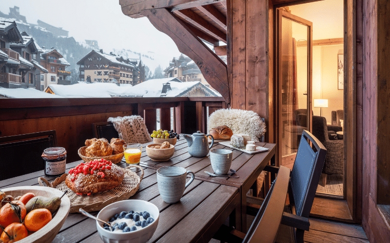Ontbijttafel staat klaar op het balkon met uitzicht over besneeuwde daken en bergen