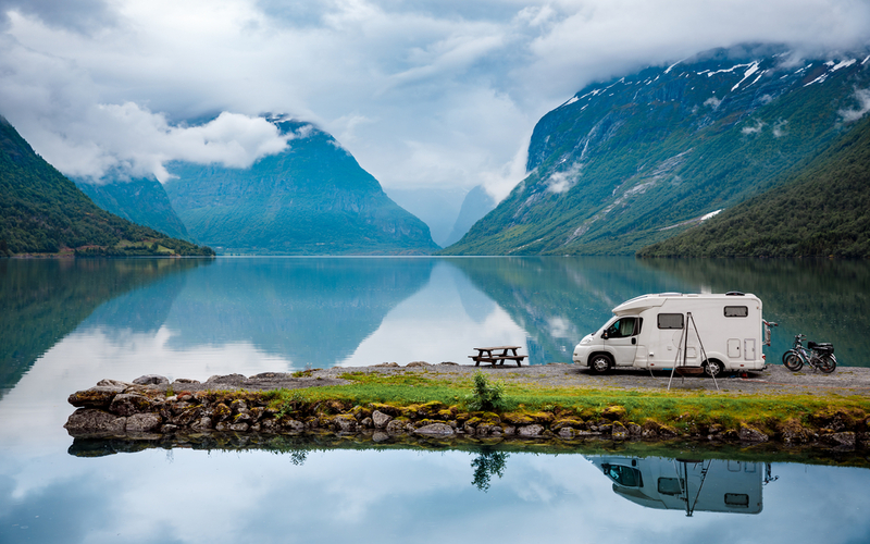 Geparkeerde caravan naast groot meer in bergachtig dal met wolken