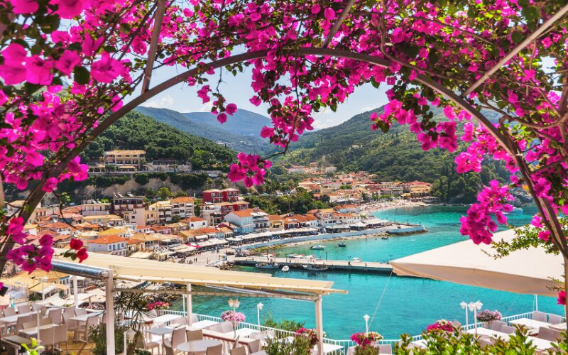 doorkijk tussen roze bloemen naar een uitzicht op de baai van Parga met de haven en turkooisblauwe zee