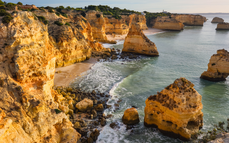 Vue du lever du soleil de la plage de Praia da Marinha en Algarve, au Portugal, avec des falaises dorées, des jetées, des vagues atlantiques, une eau turquoise et une crique rocheuse.